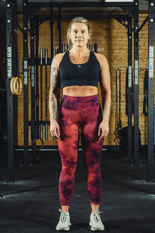 A person wearing red cloud patterned leggings and a black sports bra, standing in a gym setting.